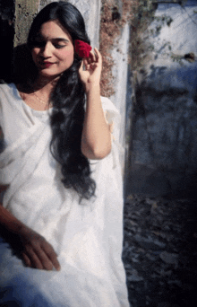 a woman in a white dress is holding a red flower in her hair