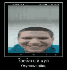 a man in a blue shirt is smiling in front of a phone screen with russian writing on it