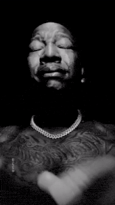 a black and white photo of a shirtless man with his hands folded and a tear coming out of his eye