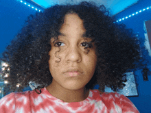 a girl with curly hair wearing a red and white tie dye shirt