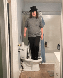 a man wearing a hat and glasses stands on the toilet