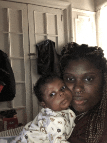 a woman holds a baby in front of a closet with a box of hige diapers