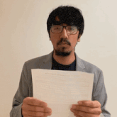 a man with glasses and a beard is holding a piece of paper in his hands