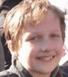 a young boy is smiling for the camera while wearing a black jacket .