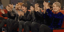 a group of people are sitting in a row clapping their hands .