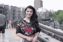 a woman in a floral top is standing in front of a train track with the name mate errori on the bottom