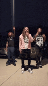 three people are standing in front of a car and one of them has a shirt that says " i 'm a rapper "