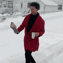 a man in a red robe is holding a book and a cup of coffee while walking in the snow