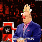 a man in a suit and tie is wearing a reindeer headband and a red nose and wishing merry christmas .