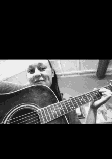 a woman is holding an acoustic guitar and smiling in a black and white photo