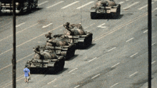 a man in a blue shirt stands in front of a row of tanks with the letters t on them