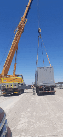 a large yellow crane is lifting a container from the back of a trailer