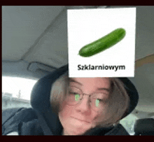 a woman wearing glasses and a black hoodie has a picture of a cucumber on her face .