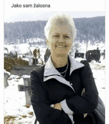 a woman in a black jacket stands in front of a cemetery with her arms crossed