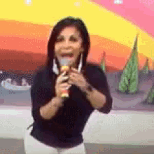 a woman is singing into a microphone while standing in front of a painting .