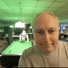 a man sitting in front of a pool table with a green light behind him