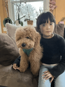 a little girl is sitting on a couch with a brown dog