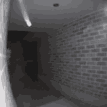 it is a black and white photo of a hallway with a brick wall .