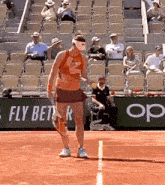 a woman is holding a tennis racquet on a tennis court in front of a sign that says fly better op