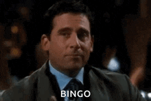 a man in a suit and tie is holding a glass of wine and saying `` bingo '' .