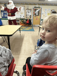 a little girl sits in a red chair in front of a man dressed as santa