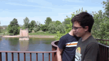 two young men are standing on a bridge overlooking a river and one of them is wearing a shirt that says california