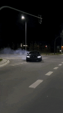 a black car is driving down a street at night with smoke coming out of the tires