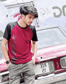 a young man standing in front of a red car with a license plate that says 3181