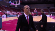 a man in a suit and tie walks on a basketball court with a sign that says " aseguramos lo que está por venir "