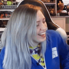 a woman in a blue jacket is smiling and laughing while sitting in front of a shelf with toys on it .