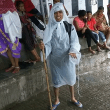 a man in a raincoat holds a cane in front of a crowd of people