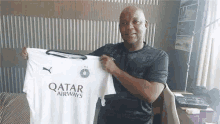 a man is holding a white qatar airways jersey in his hand .