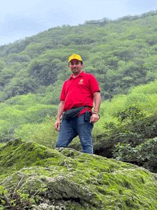 a man in a red shirt and yellow hat stands on a rocky hillside