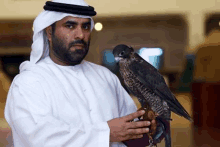 a man in a white robe is holding a falcon in his hand .