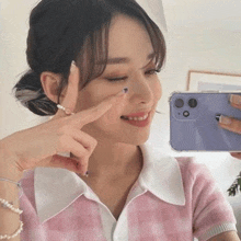 a woman is taking a selfie in front of a mirror while holding a purple phone .