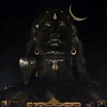 a statue of lord shiva with a crescent moon on his head is lit up at night .