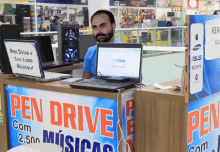 a man sits behind a counter that says pen drive com 2.500 musicas