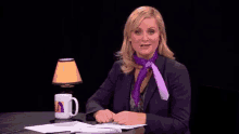 a woman wearing a purple tie sits at a desk with a lamp and a mug with a woman on it