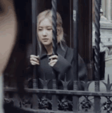 a woman is standing behind a fence holding onto a metal bar .