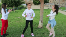 three young girls are dancing in a park and one of them is wearing a sweatshirt that says never give up .