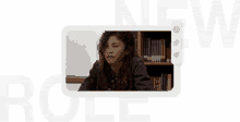 a woman is sitting at a table in front of a bookshelf .