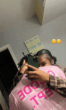 a woman is taking a picture of herself in a mirror while wearing a pink shirt that says ' code ' on it