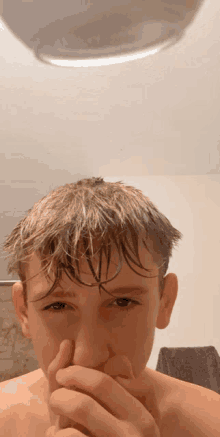 a young boy with wet hair is covering his mouth with his hands