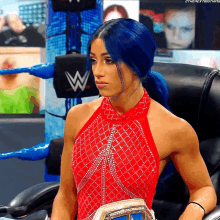 a woman with blue hair is wearing a red dress and holding a wrestling championship belt