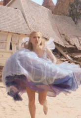 a woman in a blue dress is running in front of a destroyed house