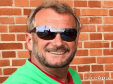 a man wearing sunglasses and a green shirt is standing in front of a brick wall