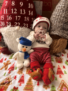 a baby wearing a santa hat holds a stuffed snowman in front of an advent calendar