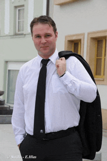 a man wearing a white shirt and a black tie is standing in front of a building