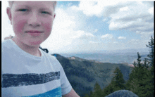 a boy in a striped shirt stands in front of a mountain range