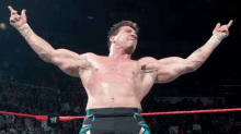 a shirtless wrestler is standing in a wrestling ring with his arms in the air .